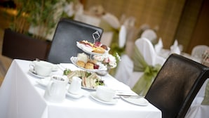 Une table dressée pour un service à thé, avec un présentoir à gâteaux à plusieurs niveaux, une nappe blanche et des décorations florales.