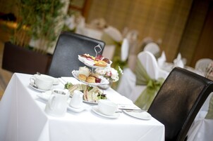 A table set for a tea service with a tiered dessert display, white tablecloth, and floral decorations.
