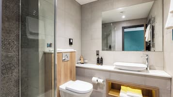 Un baño moderno con cabina de ducha de vidrio, inodoro blanco, lavamanos con espejo y toallero.