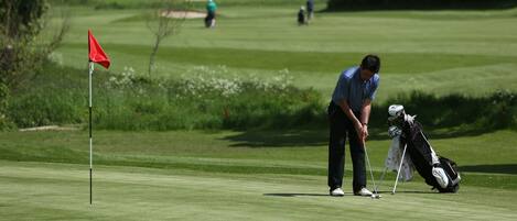 A golf course with a red flag, a golfer preparing to putt, and a golf bag.