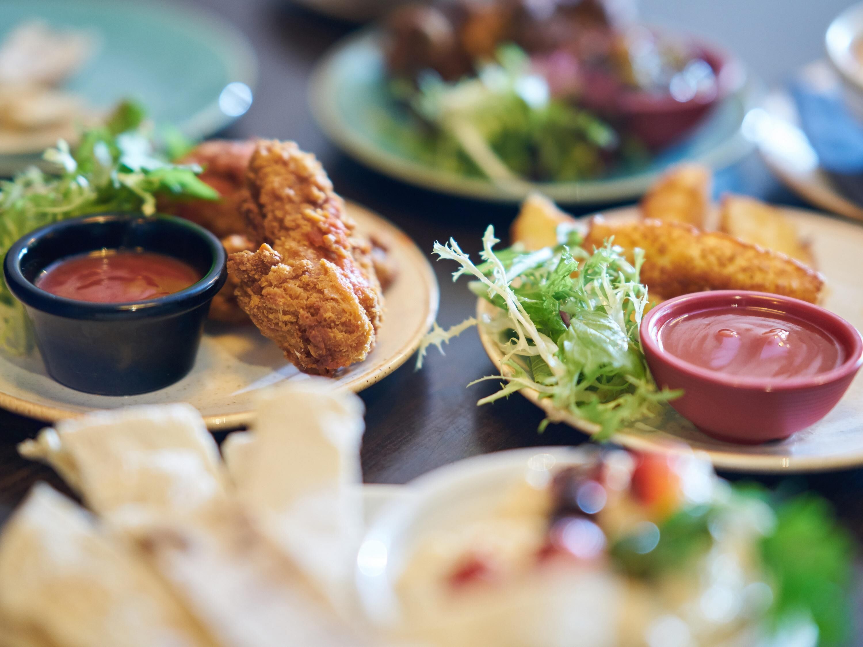 A table with plates of fried chicken, salad, and dipping sauces.