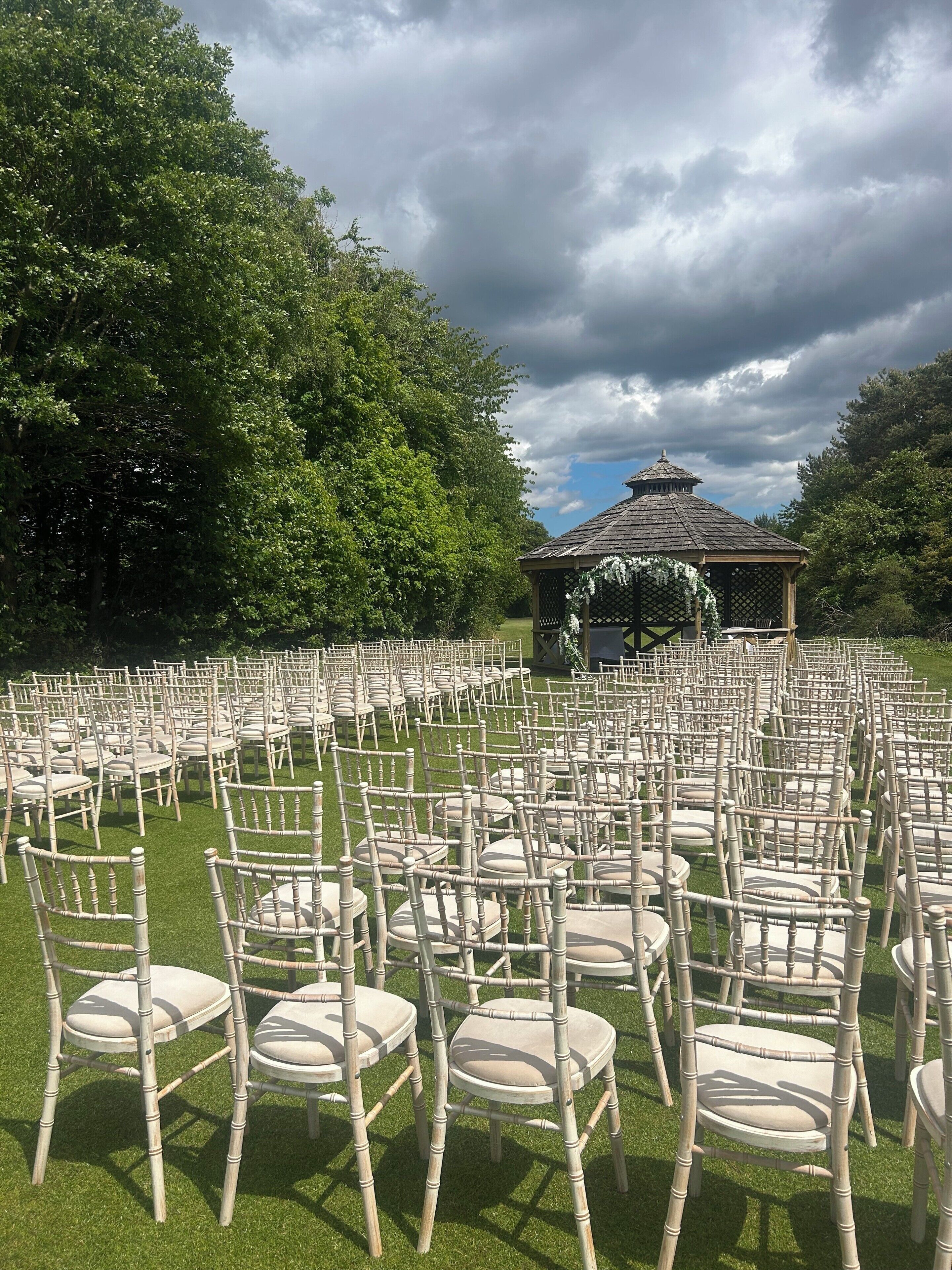 A gazebo with a tiled roof surrounded by rows of chairs on a grassy lawn.