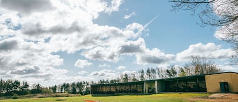 En bygning med en stor glasfacade, en græsplæne foran og træer i baggrunden.