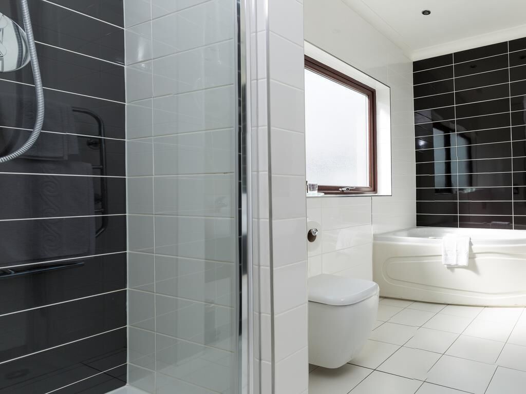 A modern bathroom with a glass shower enclosure, a white toilet, and a large bathtub.
