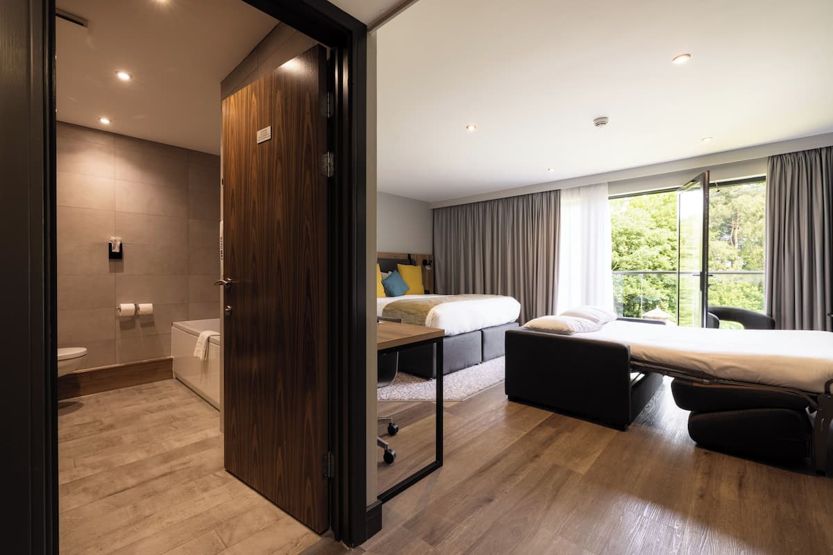 Una habitación de hotel moderna con suelo de madera, una cama, un escritorio y vistas al exterior.