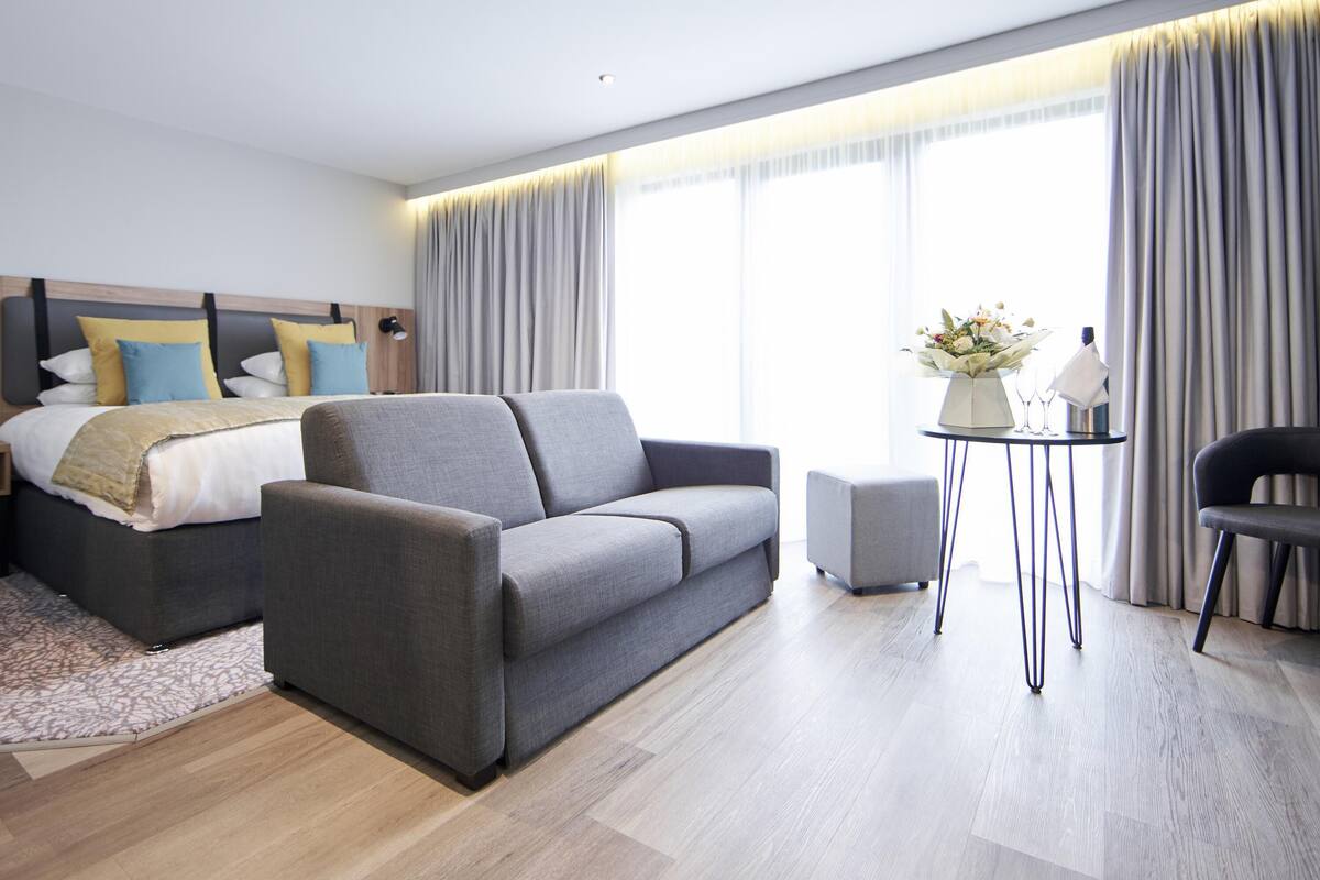 A modern hotel room with a bed, sofa, small table, and a chair.