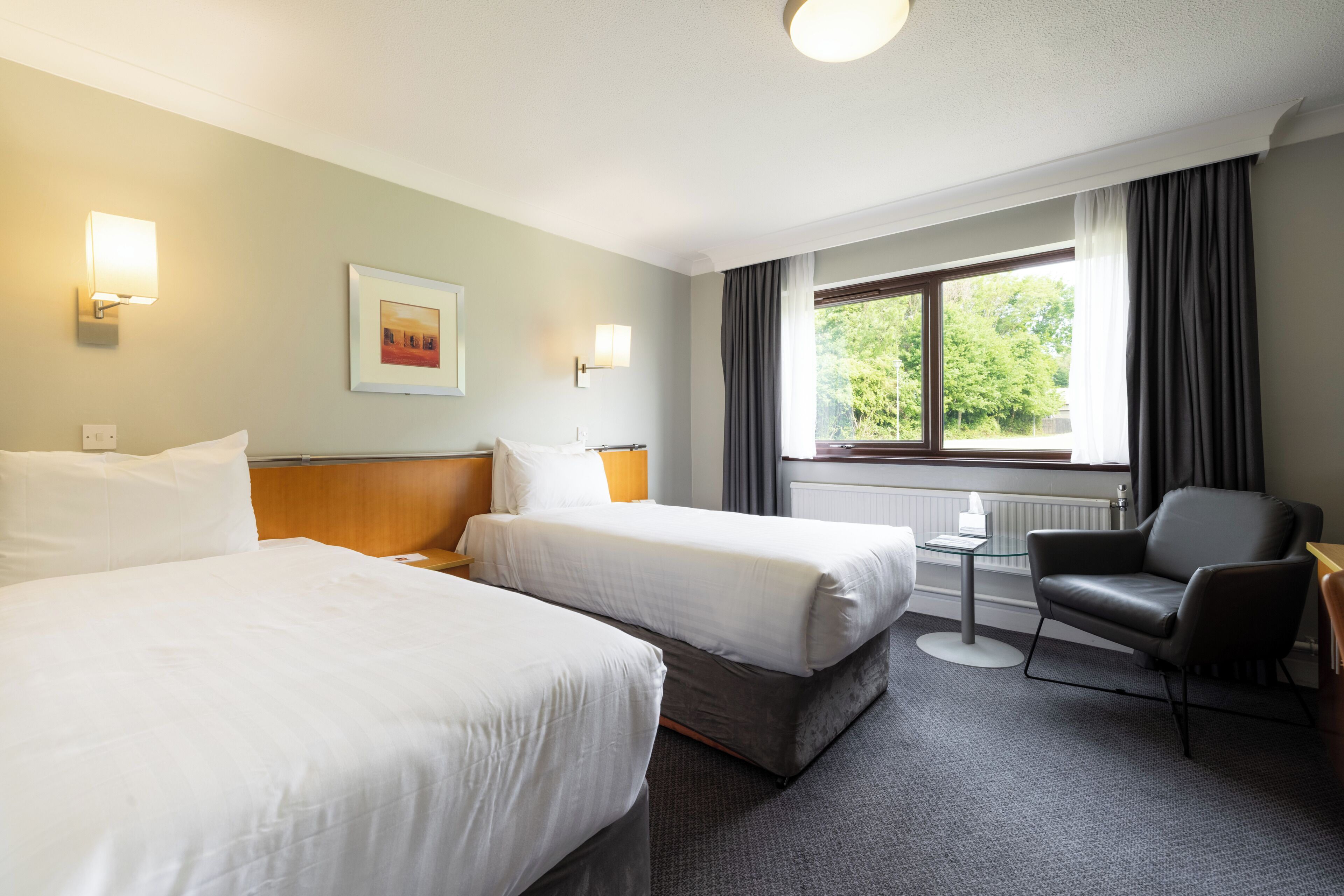 A hotel room with two beds, a desk, a chair, and a window with curtains.