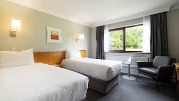 A hotel room with two beds, a desk, a chair, and a window with curtains.