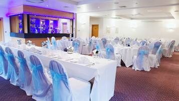 A banquet hall with round tables, white tablecloths, and chairs with blue sashes.