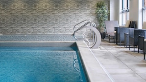 Une piscine avec un mur en pierre, un escalier métallique et un espace extérieur aménagé avec des chaises et une table.