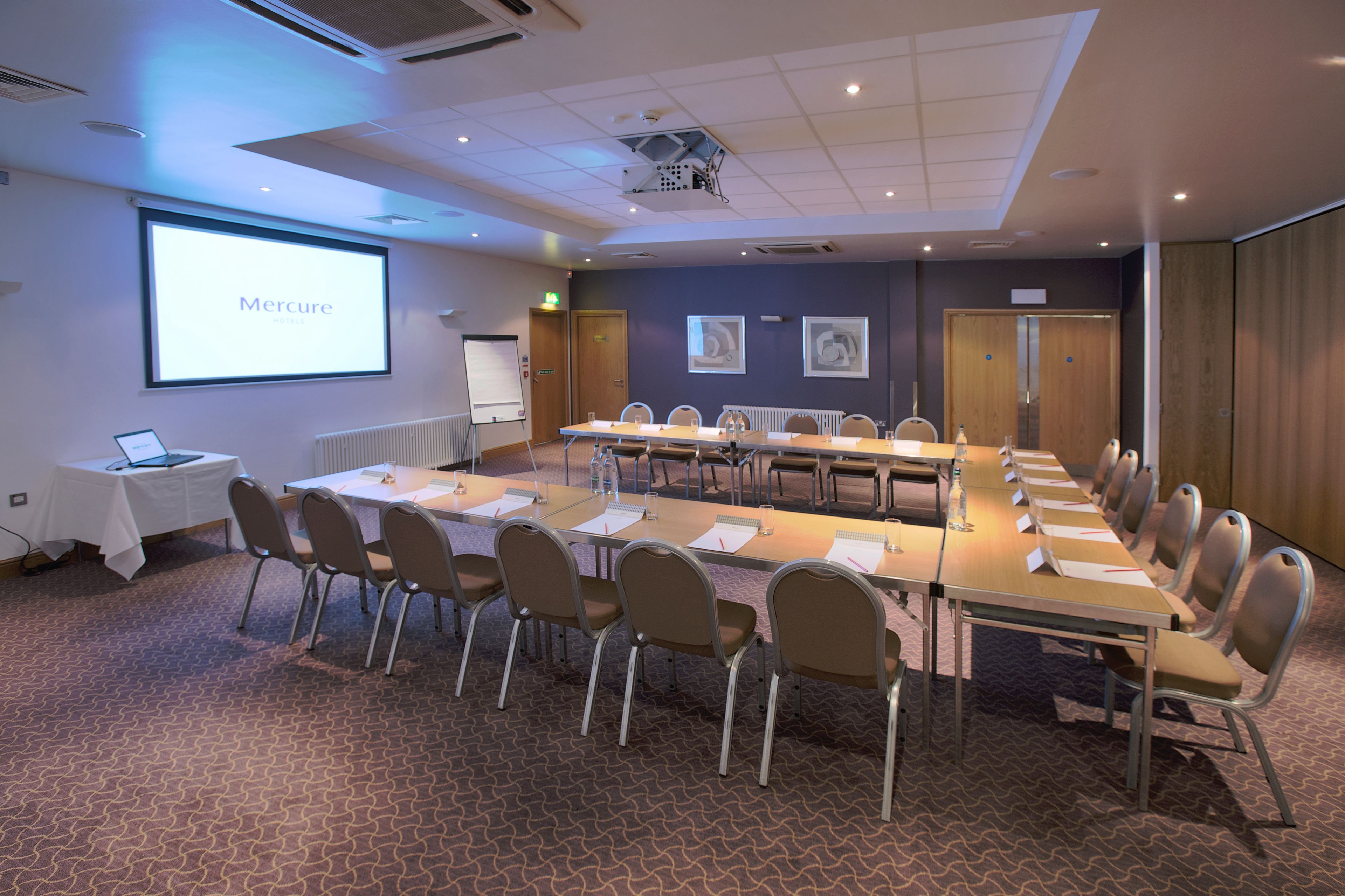 A conference room with a long table, chairs, a projector screen displaying 'Mercure', and a whiteboard.