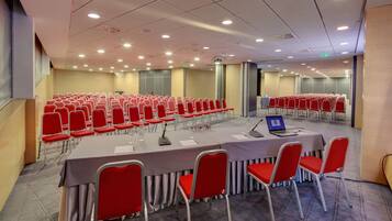 A conference room with rows of red chairs, a long table with a laptop, and a ceiling with recessed lighting.