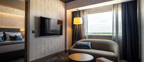 A modern hotel room with a bed, a sofa, a small table, and a TV.