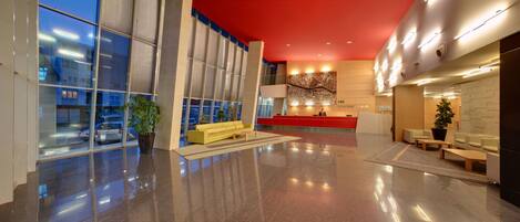 A modern hotel lobby with a reception desk, seating area, and large windows.