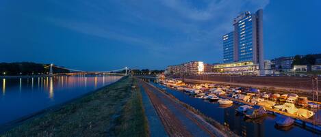 A marina with boats docked, a bridge in the background, and a tall building with multiple floors.