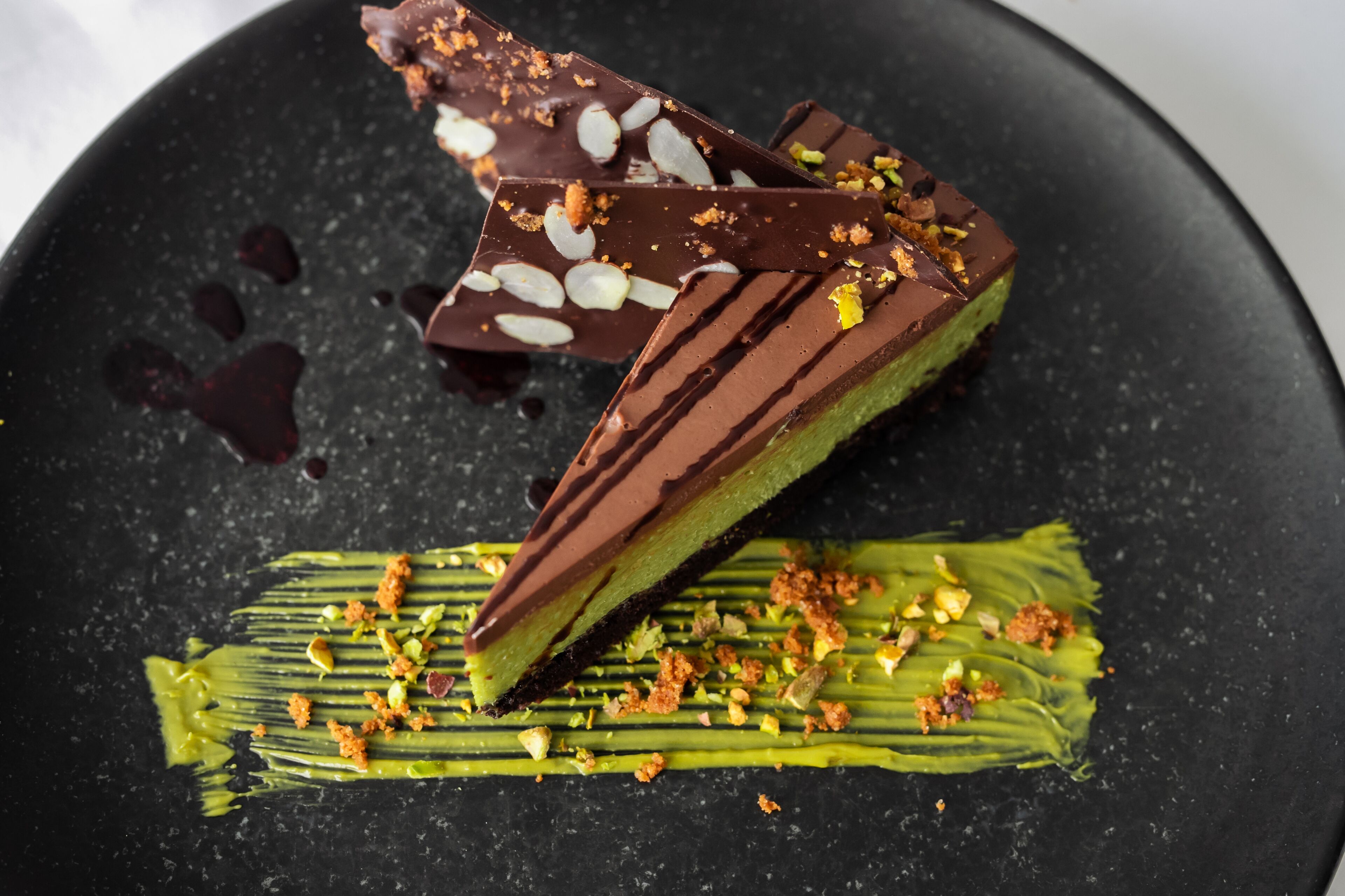 Un dessert au chocolat agrémenté d’éléments verts, présenté sur une assiette noire.