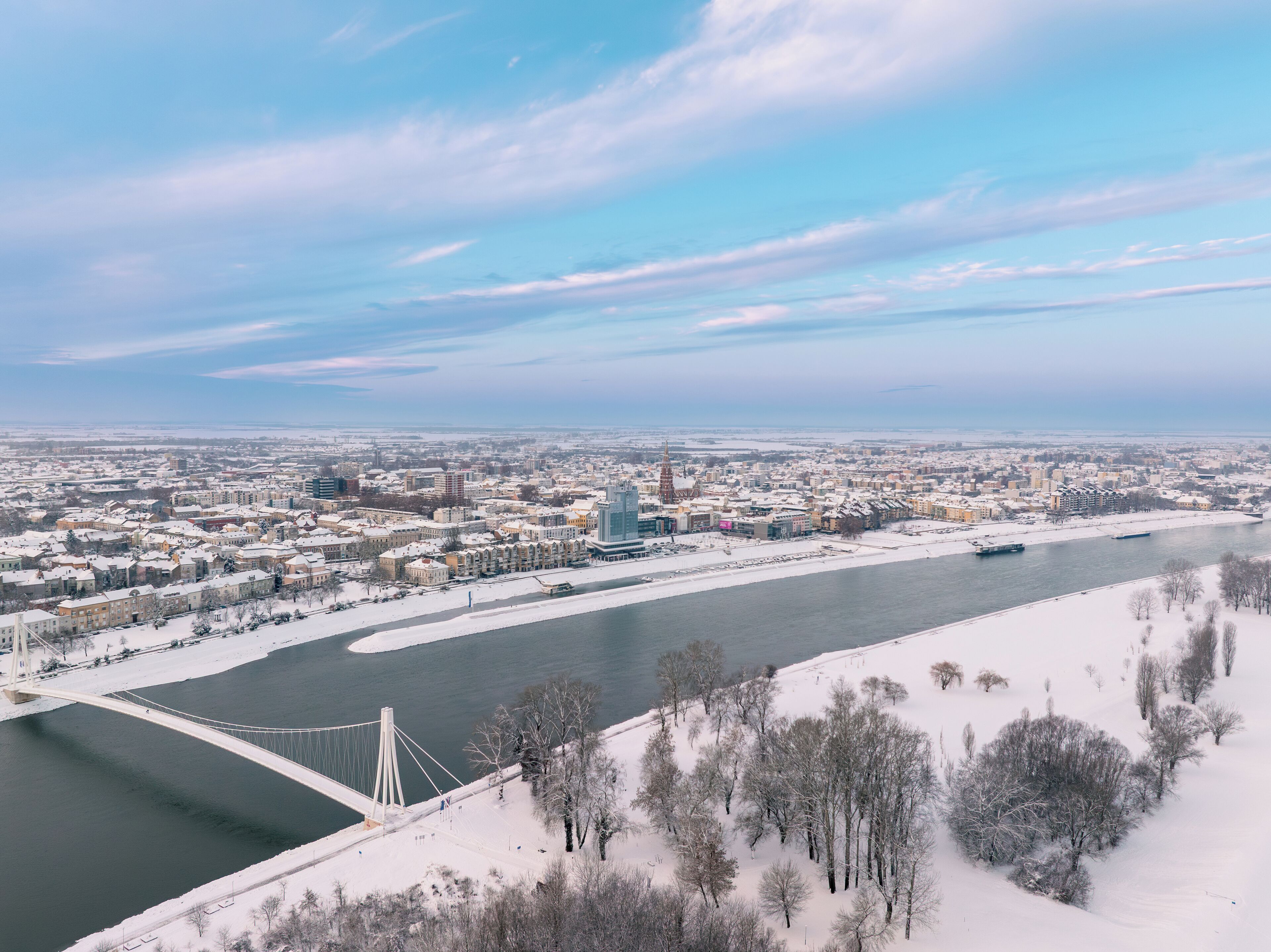 Un paisaje urbano con un río, árboles cubiertos de nieve y un puente.