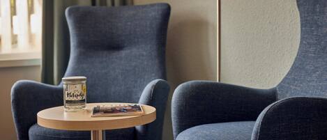 Una habitación con dos sillones azules, una mesita de madera con un tarro de crema Kiehl's y una revista.