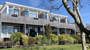 Ein zweistöckiges Haus mit einer Holzterrasse, großen Fenstern und einem gepflegten Rasen.
