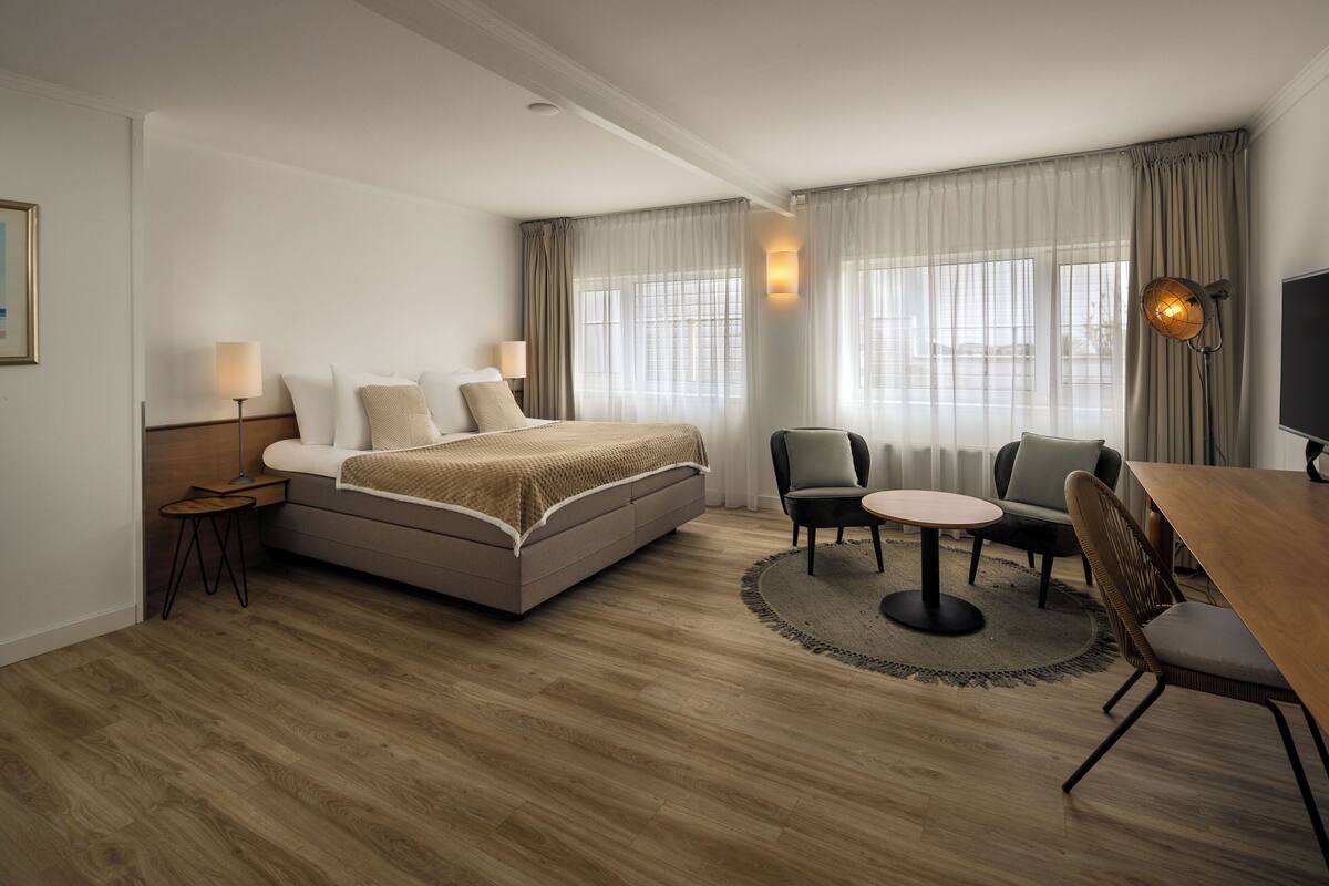 Una habitación de hotel moderna con una cama grande, una mesa de comedor, dos sillas, una mesita auxiliar y un televisor.