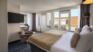 Ein Hotelzimmer mit einem großen Bett, einem an der Wand montierten Fernseher, einer Sitzecke mit Stühlen und Blick durch die Fenster nach draußen.