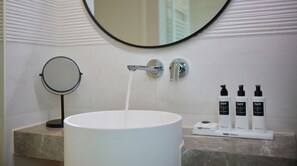 Une salle de bain avec un lavabo blanc, un miroir et trois flacons de produits de beauté de la marque FAYR posés sur le comptoir.