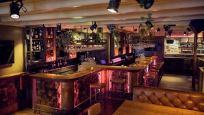 Eine Bar mit einer Holztheke, Hockstühlen und Regalen voller Flaschen und Gläser.