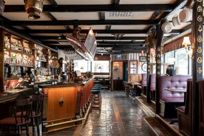 A bar with wooden bar stools, a polished stone floor, and a variety of bottles and glasses. - Hotel Bishops Arms, Köping (Köping)