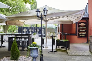 Un área de estar al aire libre con mesas y sombrillas, un letrero que dice 'The Bishops Arms', y una terraza de madera.
