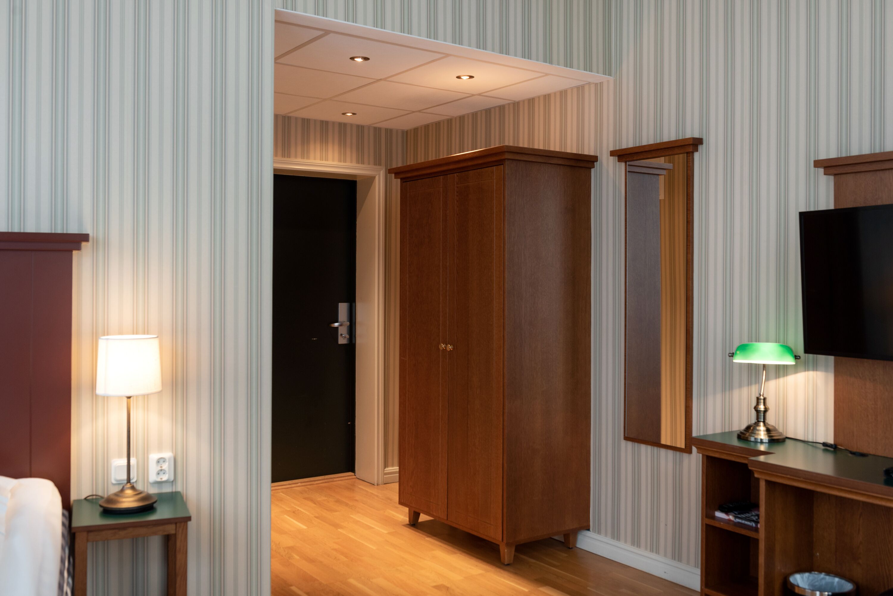 Una habitación de hotel con un armario de madera, un televisor y una lámpara sobre una mesita de noche.
