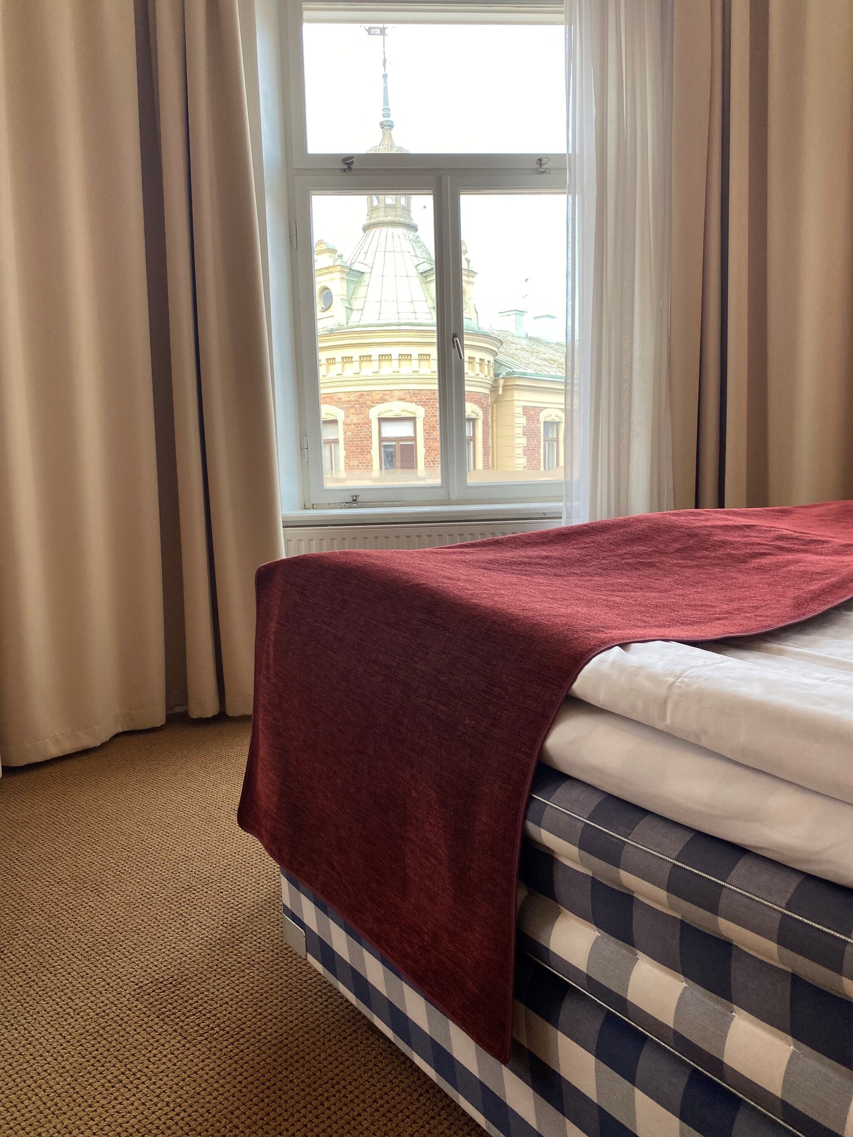 A hotel room with a bed, a window with curtains, and a view of a building with a dome and tower.