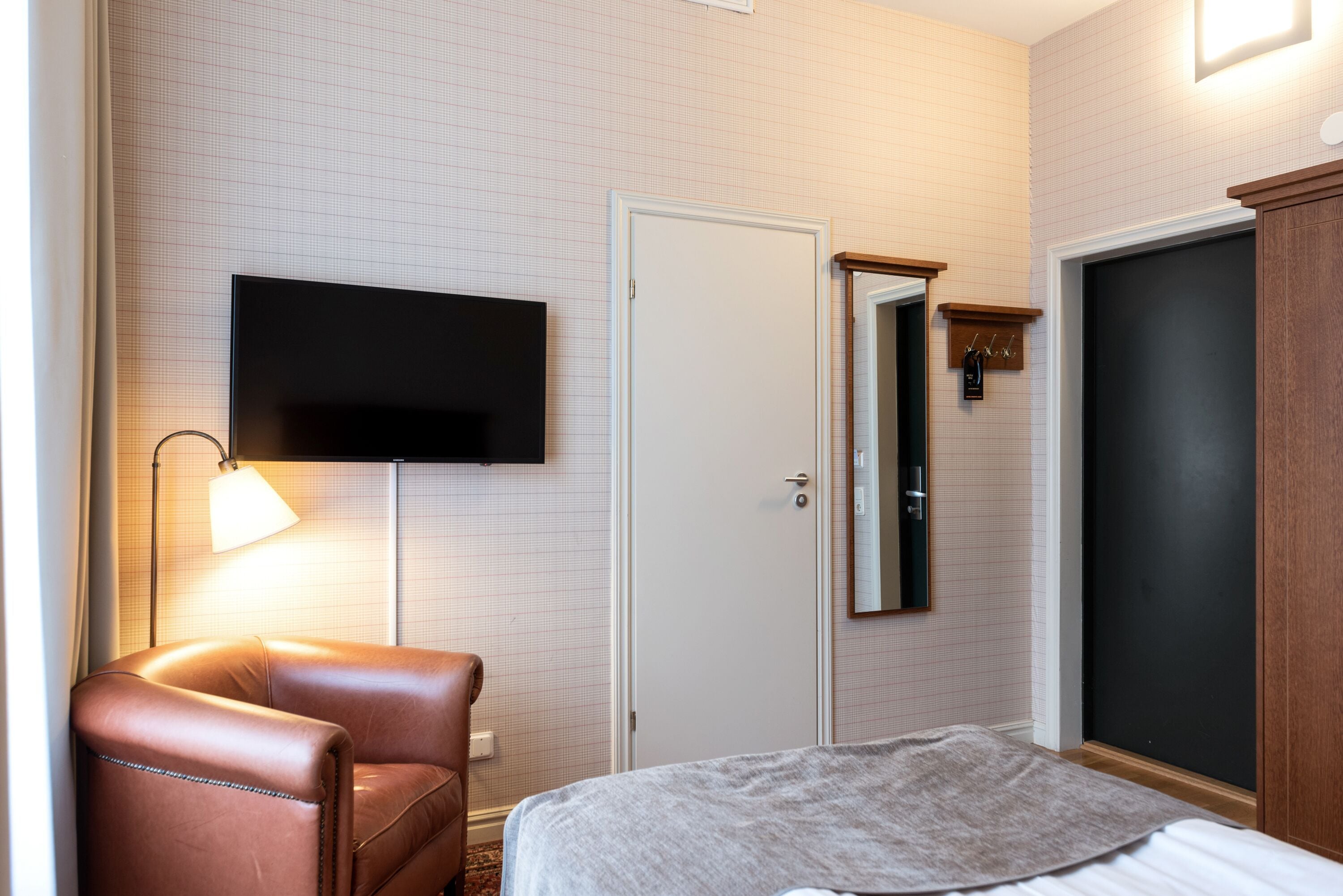 Habitación de hotel con cama, televisión montada en la pared, puerta y perchero.