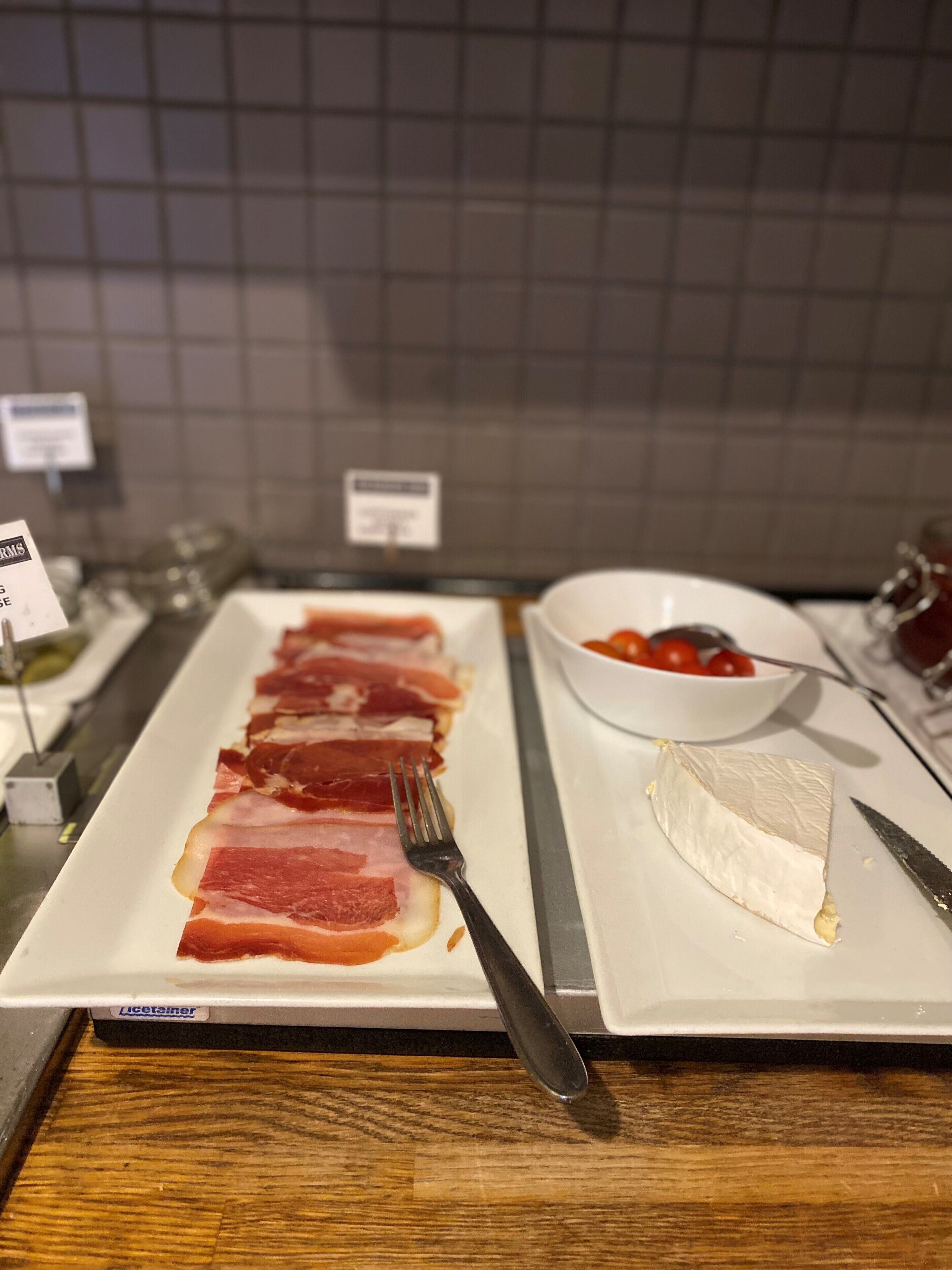 A plate of prosciutto and cheese on a wooden table with a fork and knife.