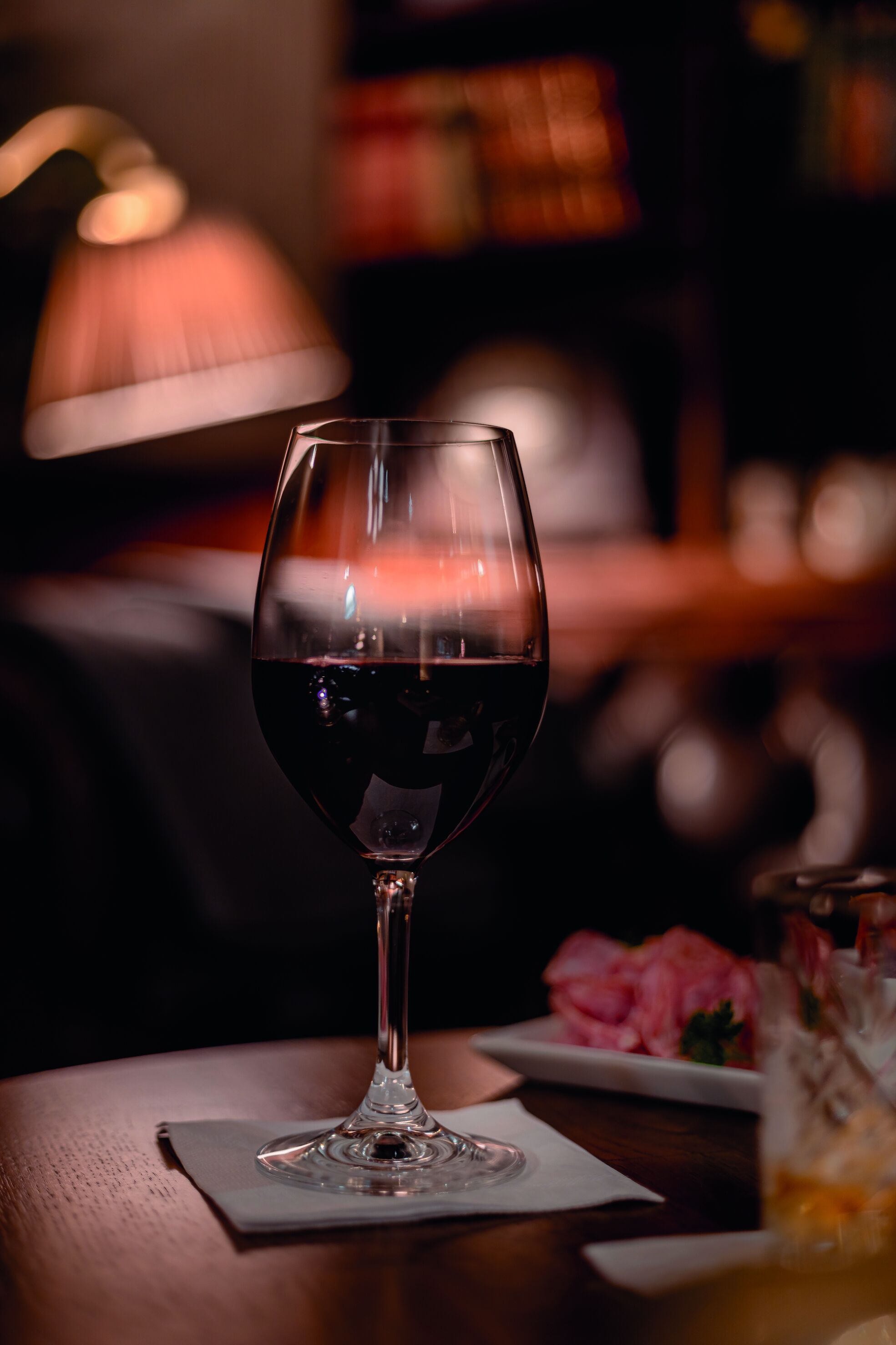 Una copa de vino sobre una mesa, con una lámpara al fondo.