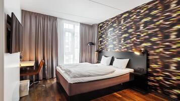 Habitación de hotel moderna con una cama grande, un escritorio con una silla y vistas a la ciudad a través de la ventana.