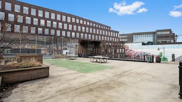 Un edificio moderno con un patio que incluye un tablero de rayuela, zonas de estar y un campo deportivo.