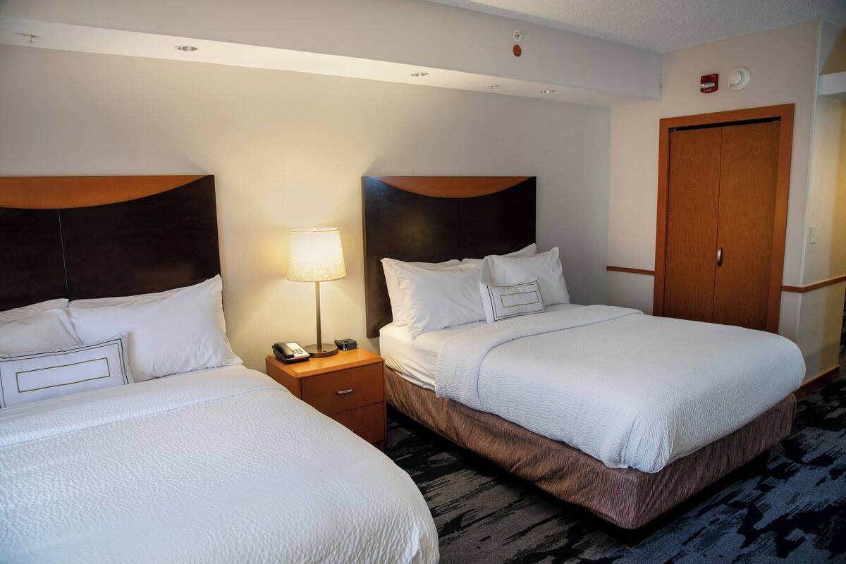 Een hotelkamer met twee bedden, een houten hoofdeinde, een nachtkastje met een lamp en een deur.