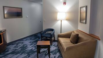 A hotel room with a blue carpet, a brown sofa, a small wooden table, a blue chair, and two framed pictures on the walls.