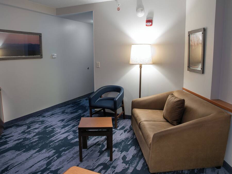 A hotel room with a blue carpet, a brown sofa, a small wooden table, a blue chair, and two framed pictures on the walls.