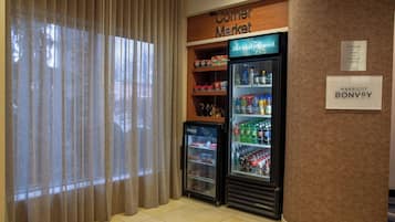 Una tienda de barrio con un refrigerador lleno de bebidas y aperitivos, un letrero de la tienda de barrio y un letrero de Marriott Bonvoy.