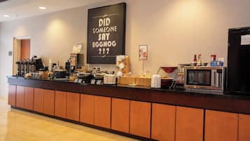 Zona de recepción de hotel con estación de café, microondas y una pizarra con un mensaje.