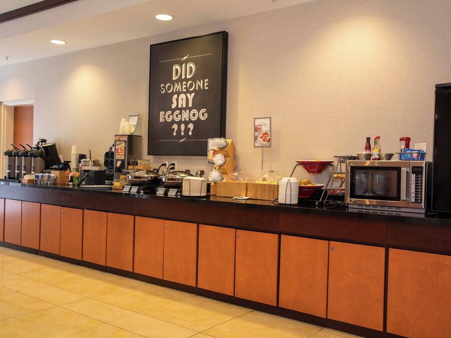 A hotel reception area with a coffee station, a microwave, and a chalkboard with a message.