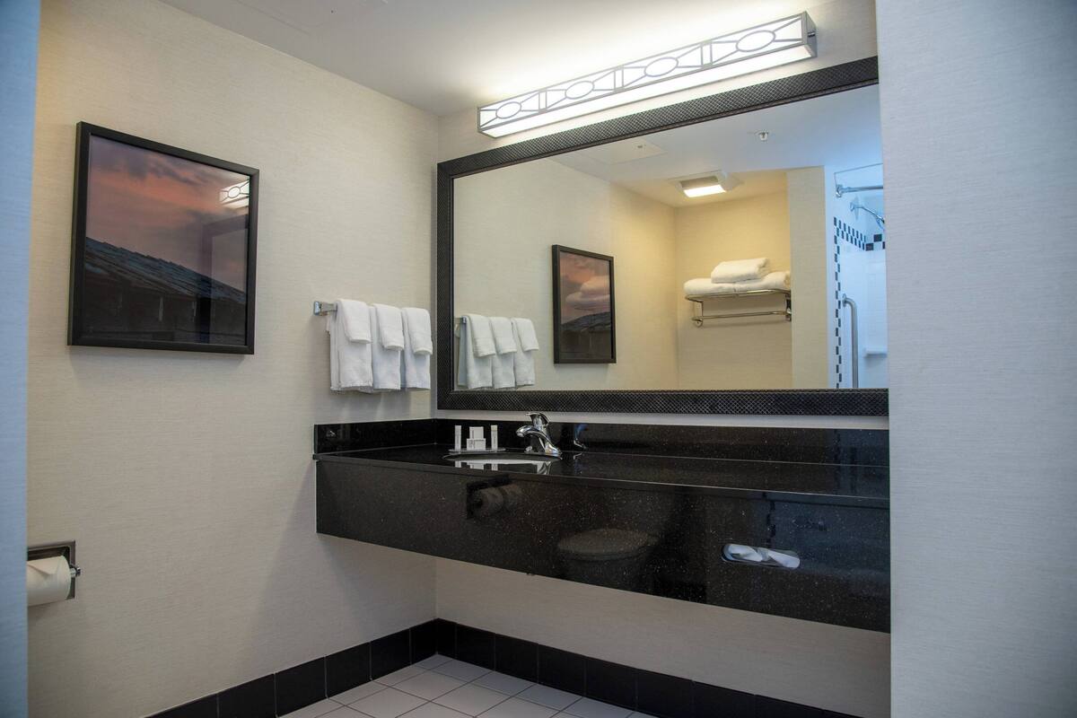 Een moderne badkamer met een zwart wastafelmeubel, een grote spiegel en witte handdoeken.