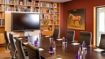 Ein Konferenzraum mit einem großen Flachbildfernseher, einer Bücherwand voller Bücher und einem Gemälde eines Pferdes an der Wand.
