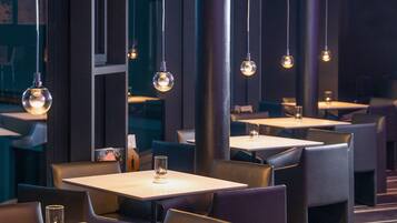 En restaurang med bord och stolar uppställda i rader, stora fönster och hängande taklampor.