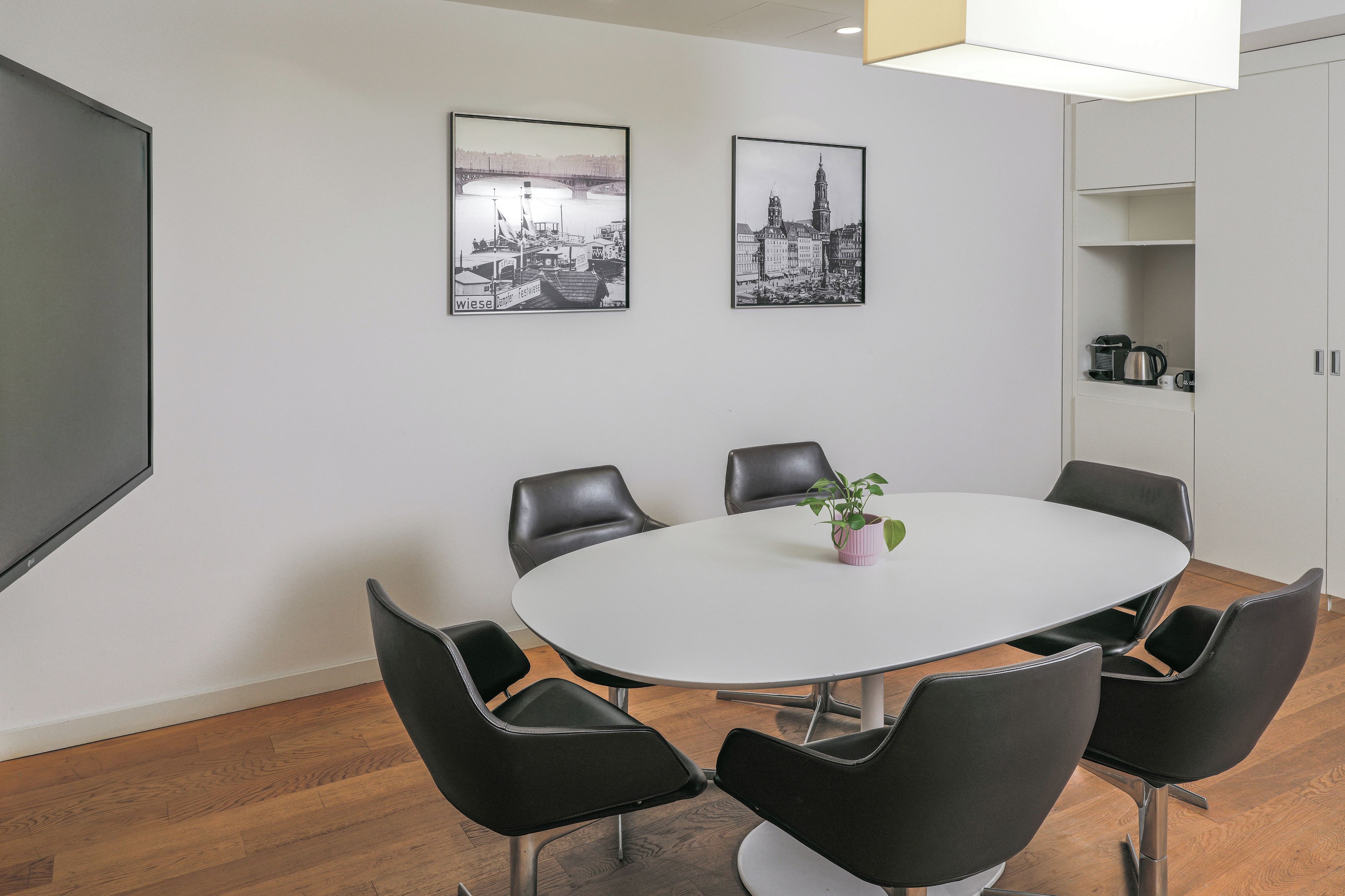 Un salón de conferencias con una mesa blanca, sillas negras y dos fotografías en blanco y negro del paisaje urbano en la pared.