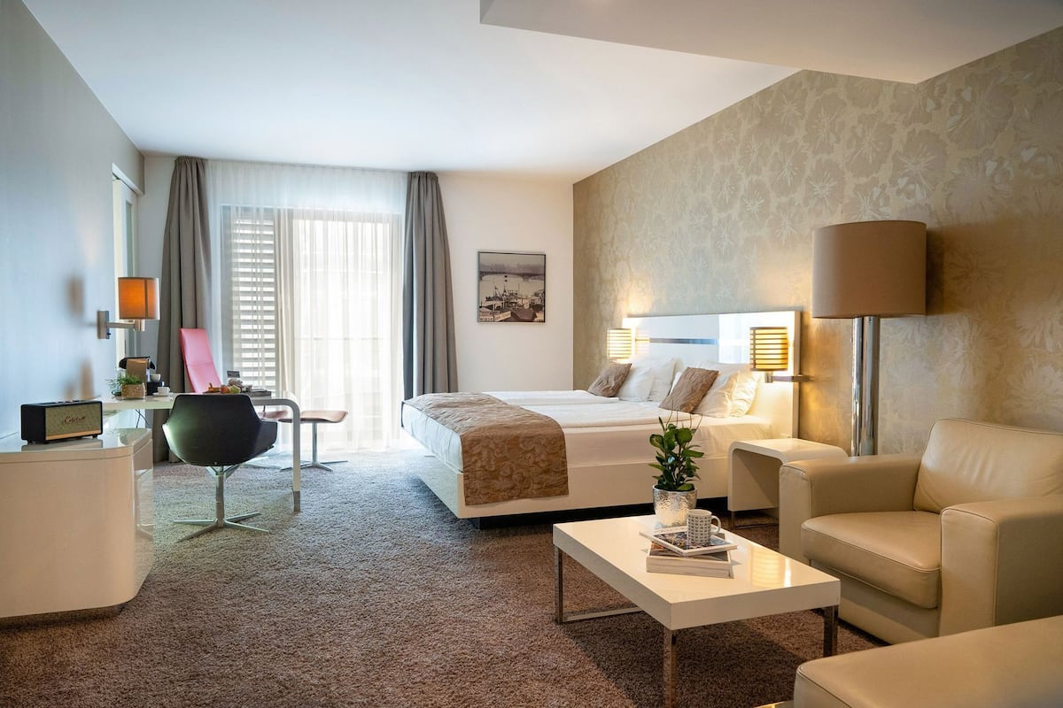 Una habitación de hotel con cama, dos mesitas de noche, un escritorio, una silla, una mesa de centro y una lámpara.