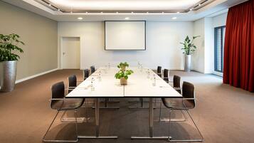 Une salle de conférence avec une longue table, des chaises, des plantes en pot et un grand écran.