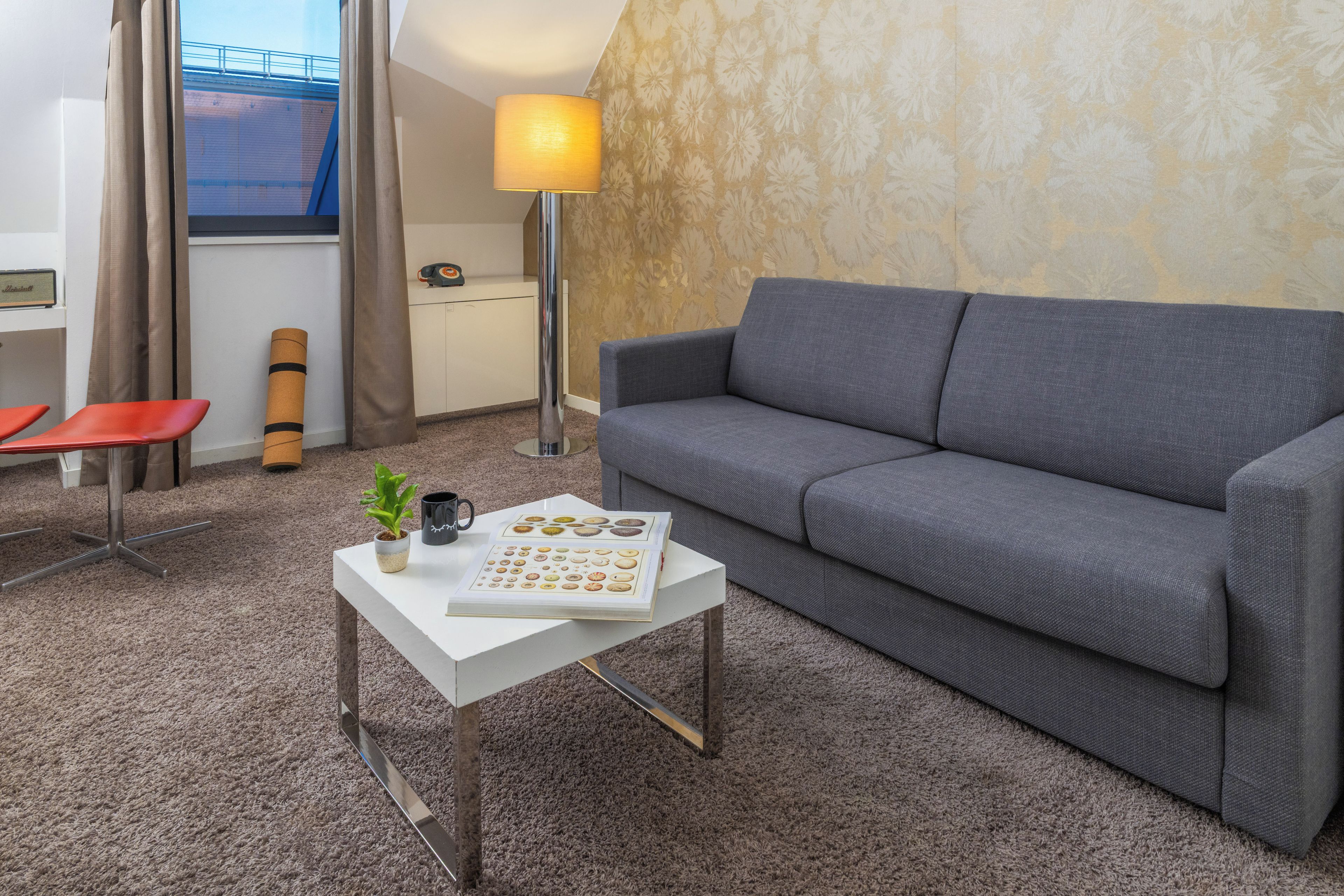 A modern living room with a grey sofa, a white coffee table with a book, a lamp, and a small plant.