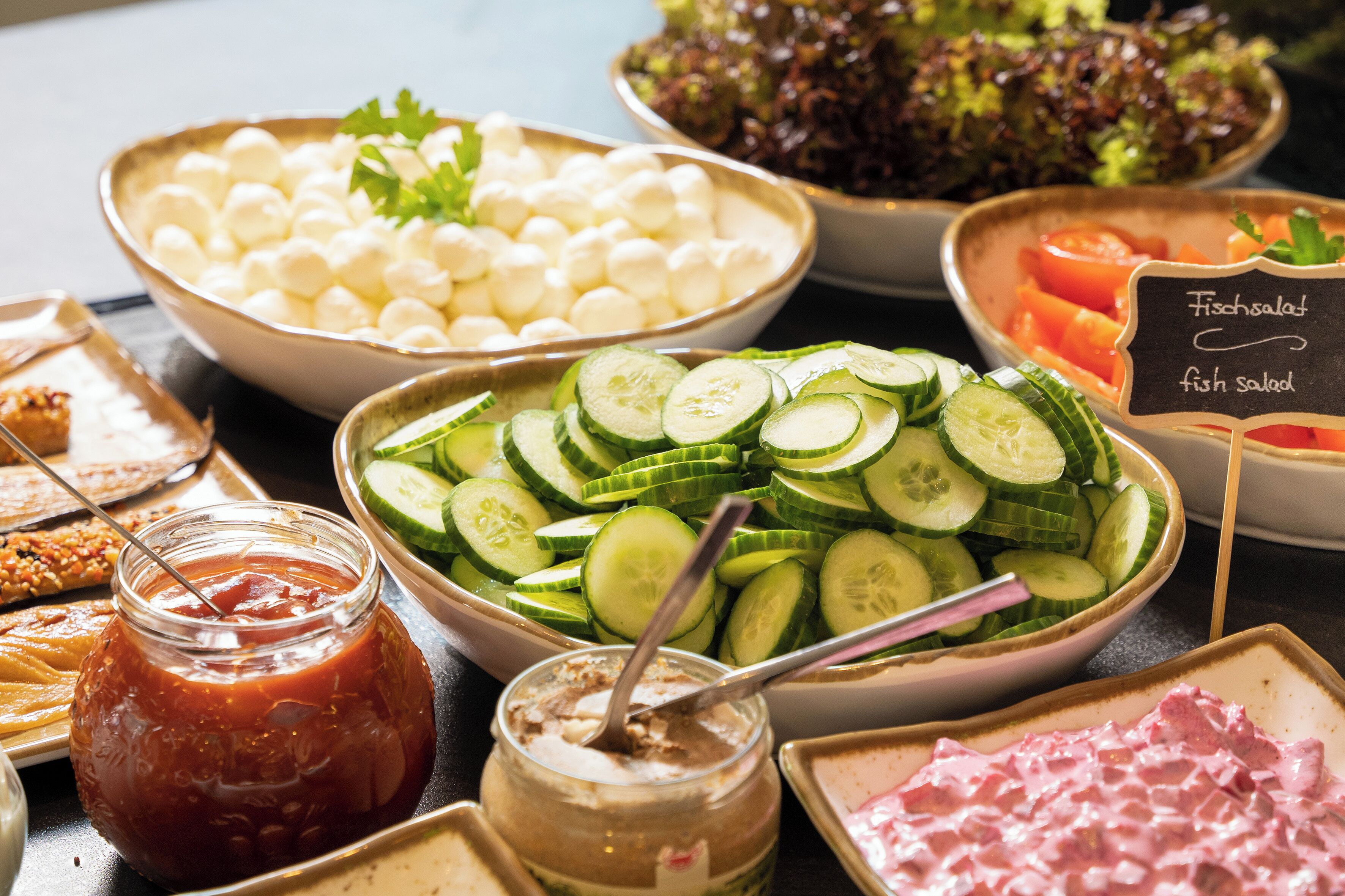 A buffet with various food options including sliced cucumbers, cheese balls, and a fish salad sign.
